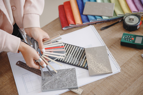 Two hands holding different color samples on a table with a notebook paper.