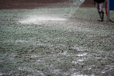This image shows a landscaping tradesperson using a hose to hydroseed a patch of soil.