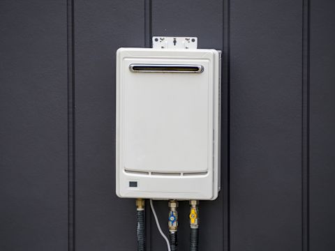 This image shows a white tankless water heater attached to an external wall with navy cladding.