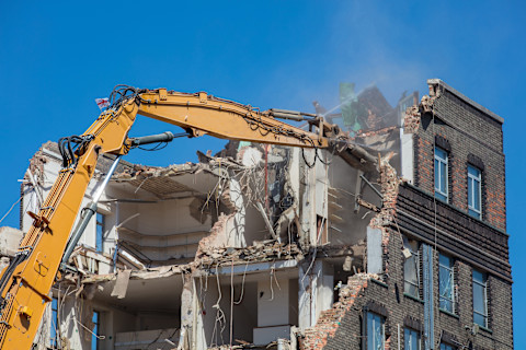 This image shows a yellow crane breaking into an apartment building, exposing the inside of the apartments. 