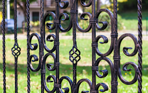 An ornamental wrought iron fence with decorative metal details is shown. The fence features classic patterns and dark metal tones.