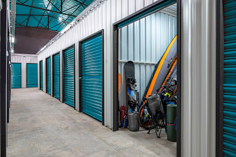 Storage units in a modern indoor facility, with one unit open and filled with sports equipment and personal items. Example of secure and organized self-storage solutions for personal or business use.