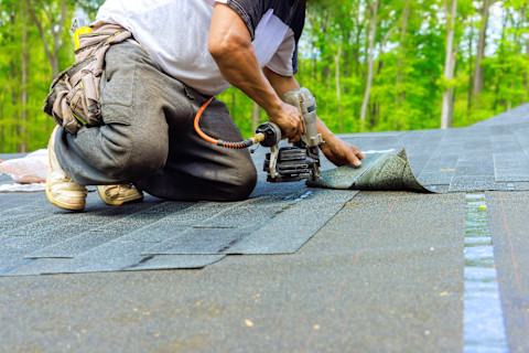 A roofer finishes installing new bitumen shingles on a roof. The shingles form a uniform surface.