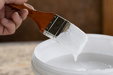A man holding a paintbrush over a tin of white paint
