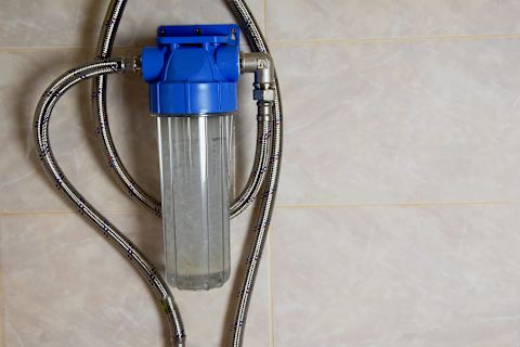 This image shows a water softener system with metal piping and a blue plastic top attached to a tiled internal wall. 