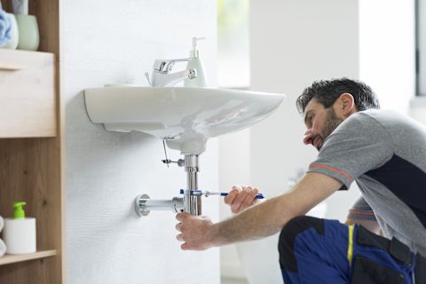 This image shows a plumber using a tool to fix a sink's pipe.