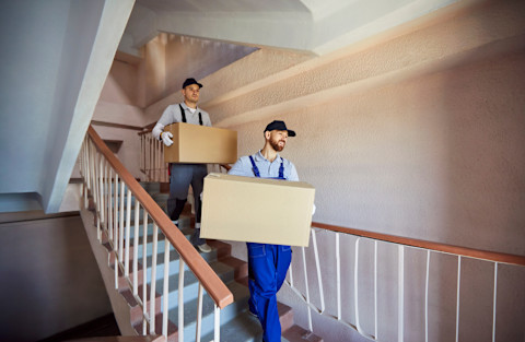Two men are carrying moving boxes down the stairs.