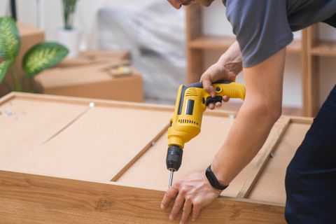 This image shows a person using a power tool to fix fasteners to a piece of custom furniture.
