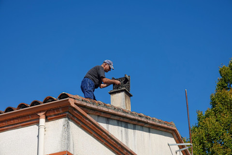 This image shows a tradesperson cleaning a chimney on a residential house.