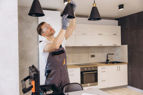 A handyman installing black lights on the ceiling of a kitchen