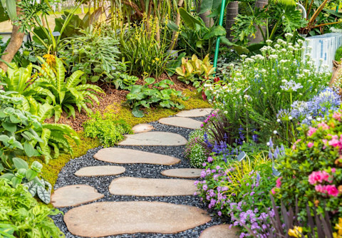 Path in the garden with tyles and pebbles, and beautiful flowers around the path