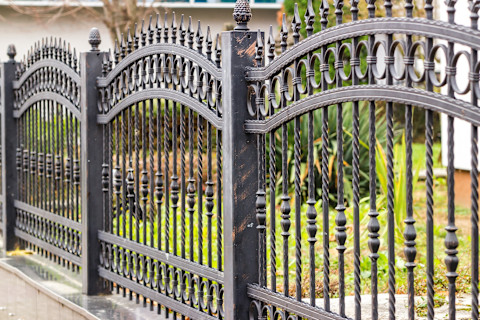 A wrought iron metal fence lines an outdoor area. The design emphasizes durability and traditional craftsmanship.