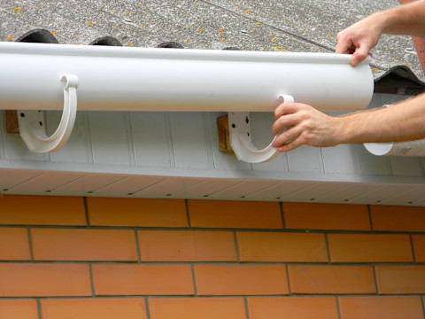 This image shows a tradesperson installing new plastic guttering on the side of a house.