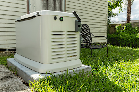 This image shows a home generator on the grass outside of a house. 