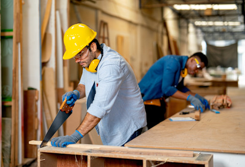 A carpenter is sawing into some wood.