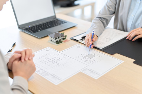 This image shows two people sat at a desk pointing at building floor plans on white pieces of paper. 