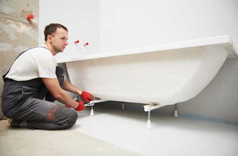 A plumber installing and mounting a new bathtub in a newly-renovated bathroom