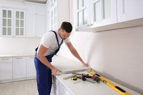 Professional kitchen countertop installation in progress, with a worker carefully positioning the surface. Example of expert craftsmanship and precision for high-quality kitchen renovations.