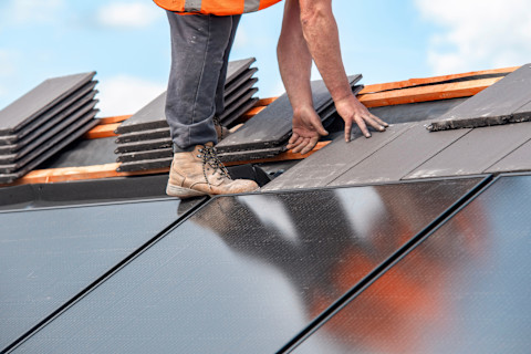 A roofing contractor installs solar panels on a residential roof. Panels are aligned in rows on the surface.