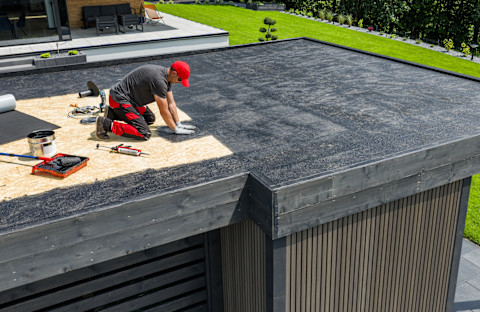 A construction worker applies EPDM roofing material on a flat roof. The rubber membrane is spread carefully across the surface.