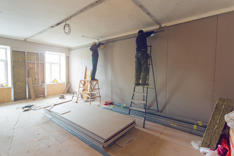 This image shows two tradespeople standing on step ladders carrying out some work at the top of a wall in a newly extended part of a home.