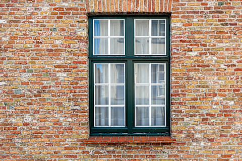 A vintage brick wall facade with a window in Bruges is shown. The aged bricks and window frame reflect historic architecture.