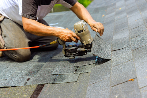 This image shows a roofer installing a new bitumen shingle on a roof. 