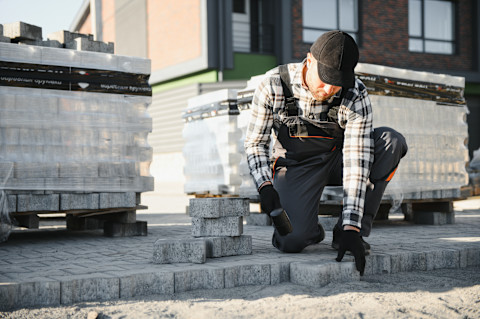 A landscaping worker installs paving stones in a garden area. 