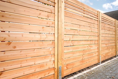 A large new wooden fence encloses a house and garden. The tall panels provide privacy and a natural look.