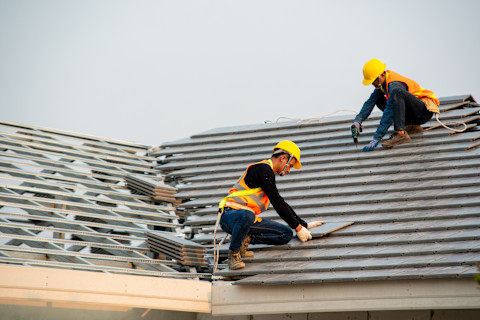 This image shows two roofers installing roofing tiles on the roof of a residential home. 