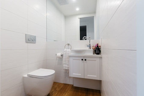 This image shows a bright and contemporary powder room with a sink, under sink cupboard, mirror and a toilet. 