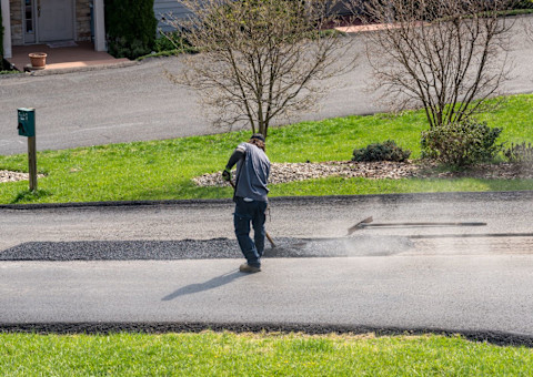 Worker applying a layer of tarmac or extra blacktop to repair damage to asphalt street
