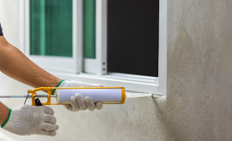 This image shows a handyman using silicone sealant caulk to seal around the edge of a PVCu window.
