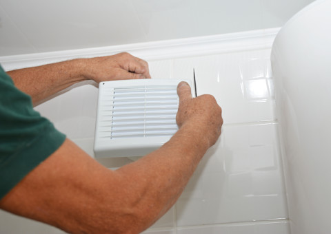 This image shows a tradesperson installing a bath fan in a tiled bathroom.