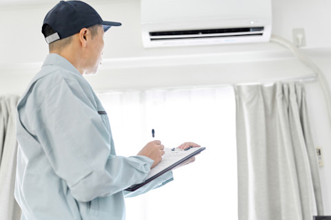 This image shows a home inspector conducting an inspection of an air conditioning system as part of a home energy audit. He is making notes on a clipboard.