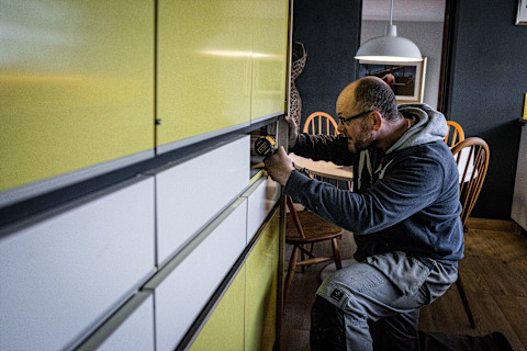 This image shows a handyman repairing a cabinet in a house.