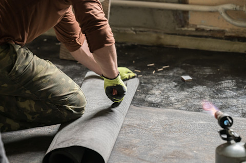 A professional handyman installing waterproofing onto the concrete floor of a basement