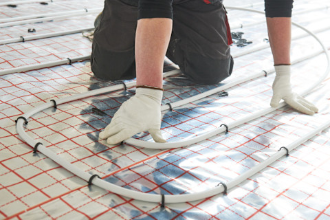 This image shows a tradesperson wearing gloves installing heated flooring