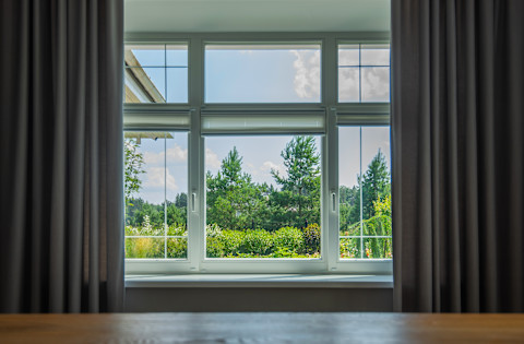 A calm outdoor view is seen through a window framed by curtains. Soft natural light creates a peaceful atmosphere.