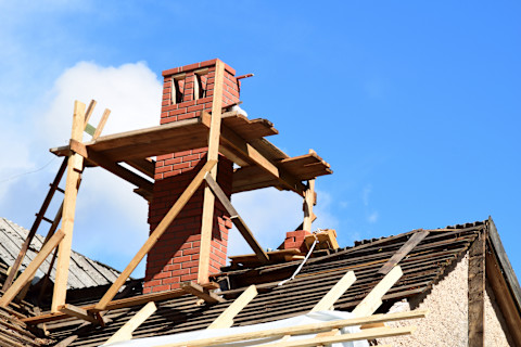 This image shows a red brick chimney surrounded by wood scaffolding as it is in the process of being repaired.