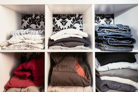 This image shows an organised wardrobe with clothes folded and stacked vertically in square compartments, showcasing a tidy and space-efficient storage system.