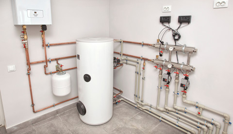 A boiler room with a lot of different equipment for a heating system, including a boiler, heater, pipes, and an expansion tank