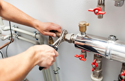 A man installs and checks a home heating system indoors. He fixes the heater components to ensure proper operation and safety.