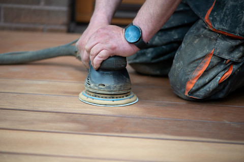 This image is a close up of a tradesperson using an electric sander to sand timber flooring.