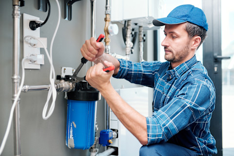This image shows a plumber using a tool to install a water filter in a home's plumbing system.