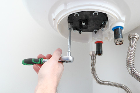 Man's hand putting a new water heater in a boiler with a screwdriver