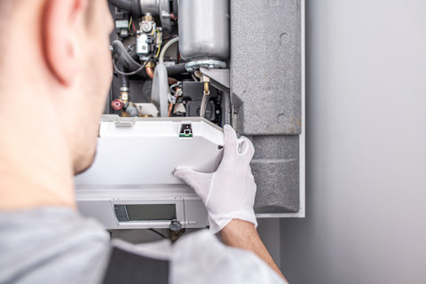 A worker wearing white gloves repairs a central heating furnace system.