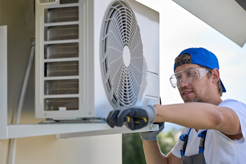 A handyman is installing an AC compressor outside
