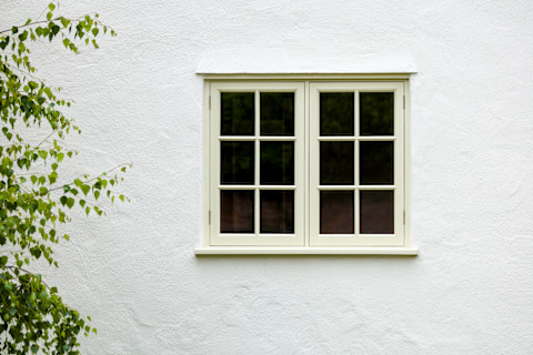 A house exterior features a wooden casement window. The window is set into a traditional brick facade.