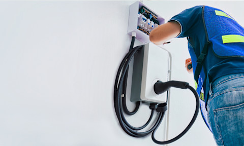 Electrician installing an electric vehicle (EV) charging station on a residential wall. EV charger setup includes electrical panel connection, cable management, and safe power supply installation. Professional EV charging station installation ensures reliable and efficient home charging for electric cars.
